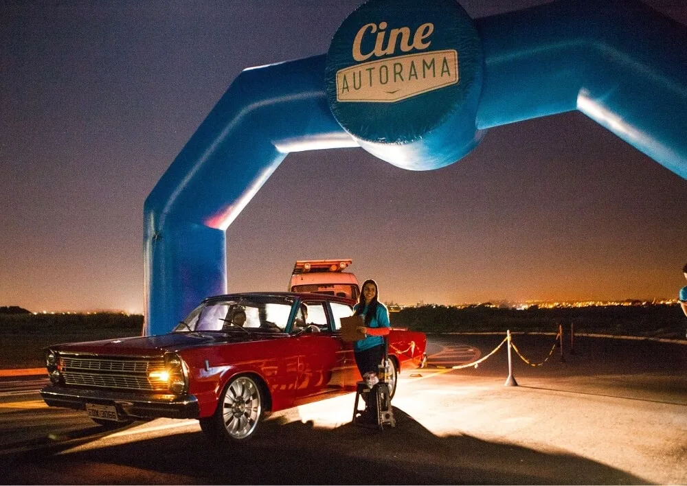 Carro clássico vermelho passando sob o arco inflável do Cine Autorama